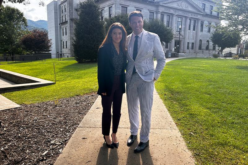 Tazanna Jones and Zeb Smathers posing for a photo on a sidewalk outside of a governmental building.